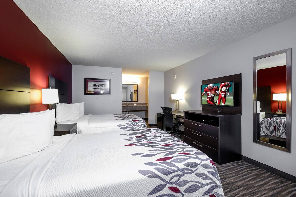 A hotel room with two beds, a desk, a TV, and a mirror.
