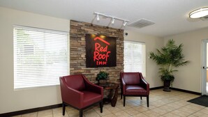 Un área de recepción con un letrero que dice 'Red Roof Inn' sobre una pared de piedra, dos sillones de cuero, una planta en maceta y un piso de baldosas.