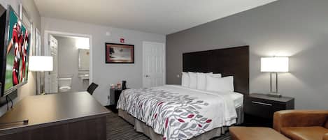 A hotel room with a bed, bedside tables, a desk, a chair, and a television.