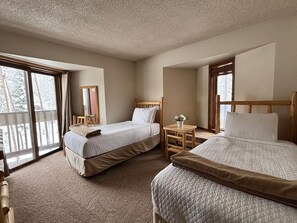 A hotel room with two beds, a small table, a chair, a mirror, and large windows with a view of trees. - Silverado II Resort & Event Center (Winter Park)