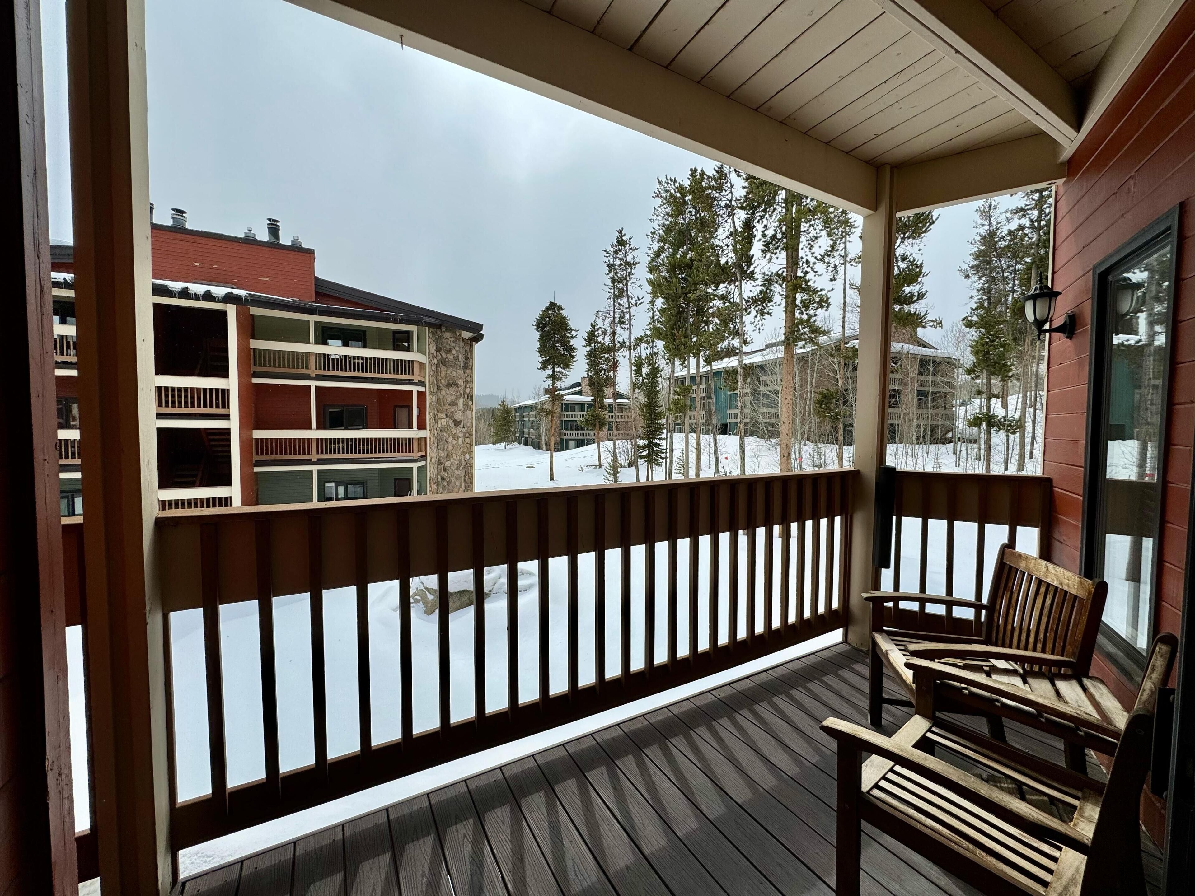 A wooden deck with a railing, two wooden chairs, and a view of a snow-covered landscape with buildings and trees.