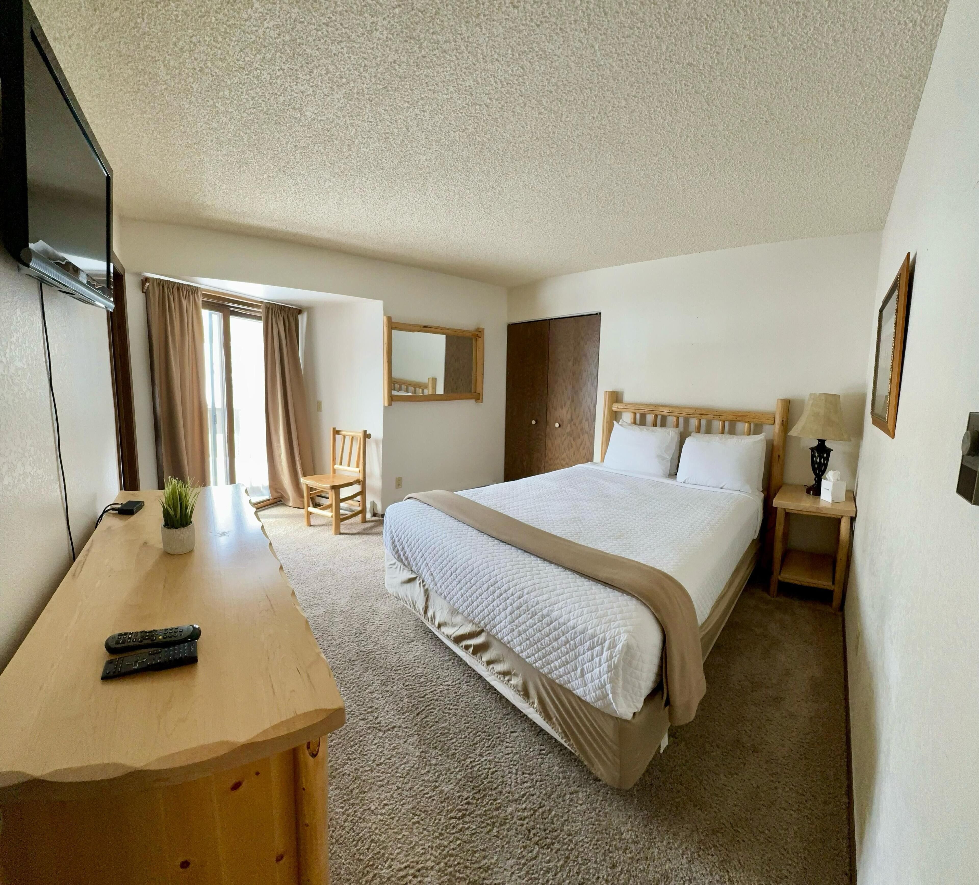A hotel room with a bed, a desk, a chair, a TV, a lamp, and a mirror.