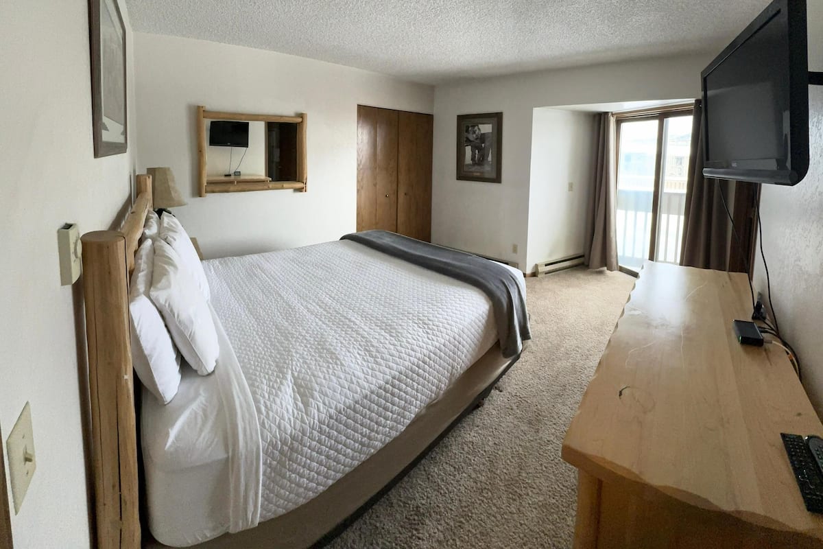 A hotel room with a bed, a desk, a TV, a window, and a door.