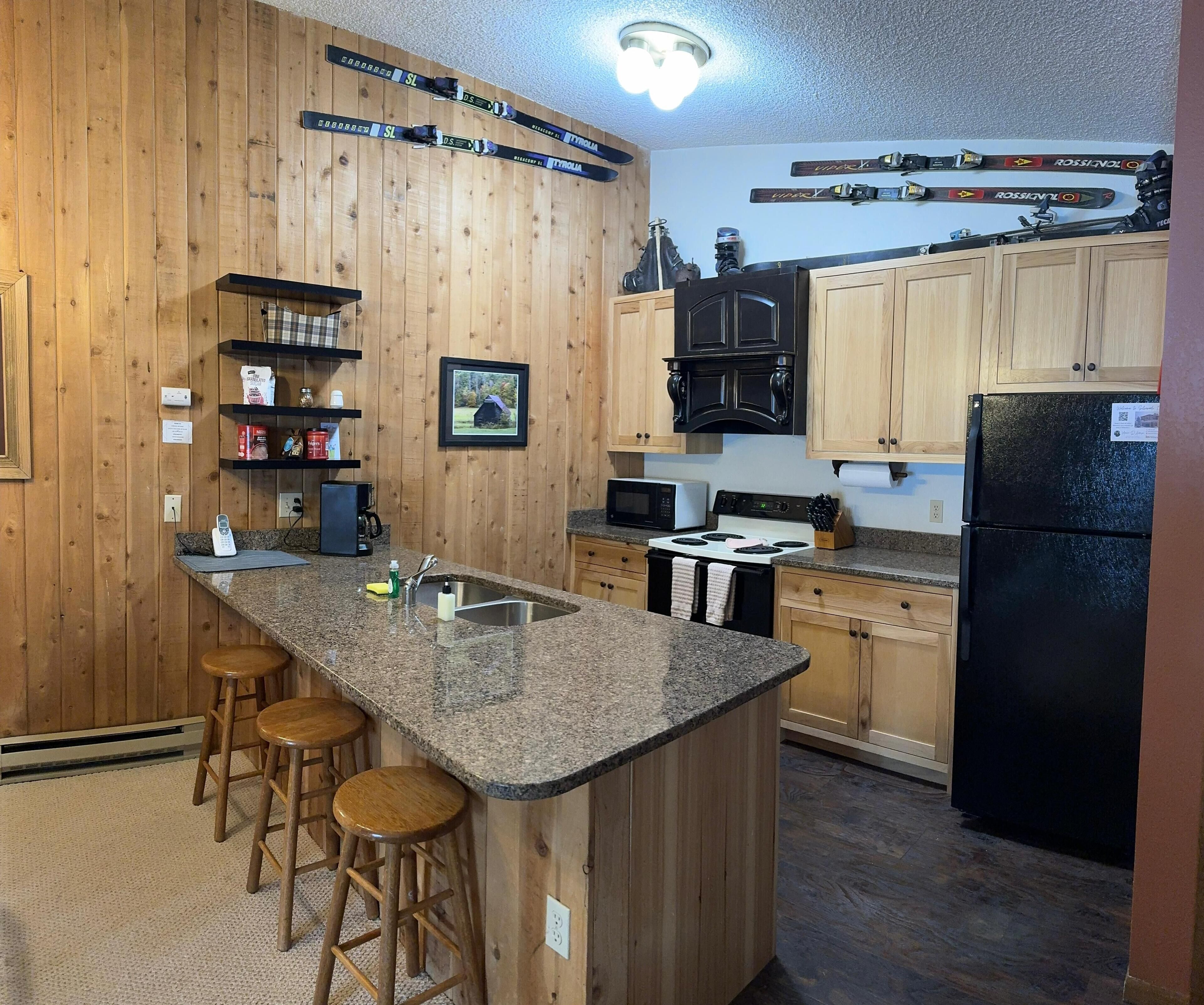 Eine Küche mit Holzschränken, einer Granit Arbeitsplatte, einem schwarzen Kühlschrank und an der Wand befestigten Skiern.