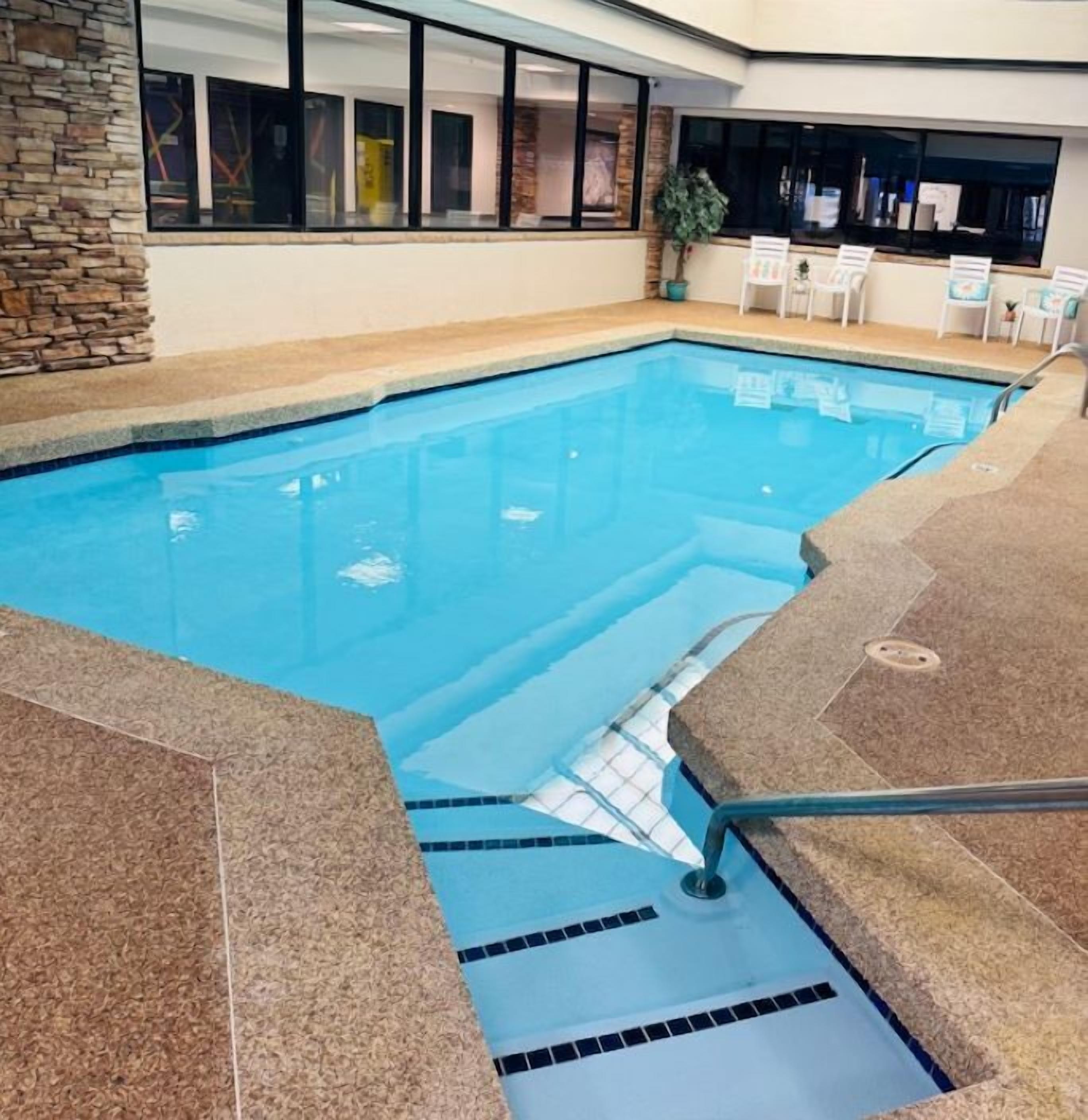 An indoor swimming pool with clear water, stone walls, and a seating area with chairs and a table.