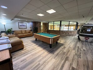 A pool table in a room with wooden flooring, a leather sofa, and a stone accent wall. - Silverado II Resort & Event Center (Winter Park)