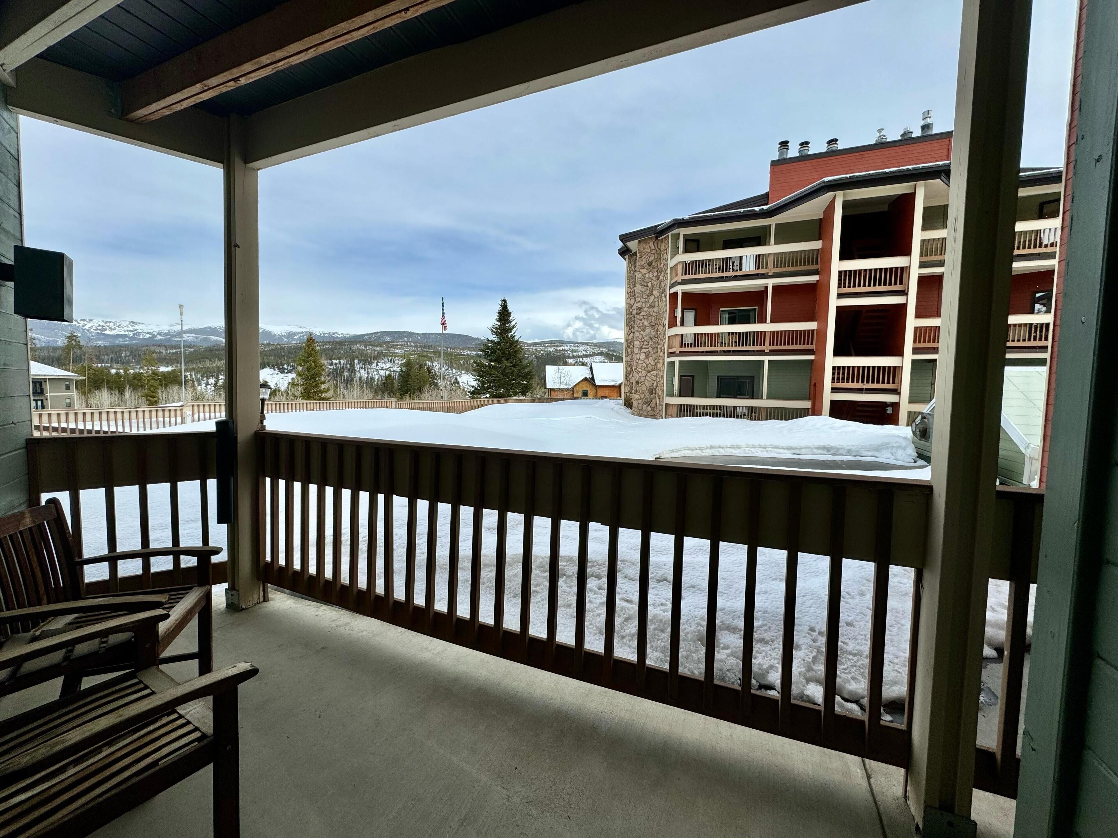 En inglasad balkong med utsikt över ett snötäckt landskap, en byggnad med flera våningar och en flagga.