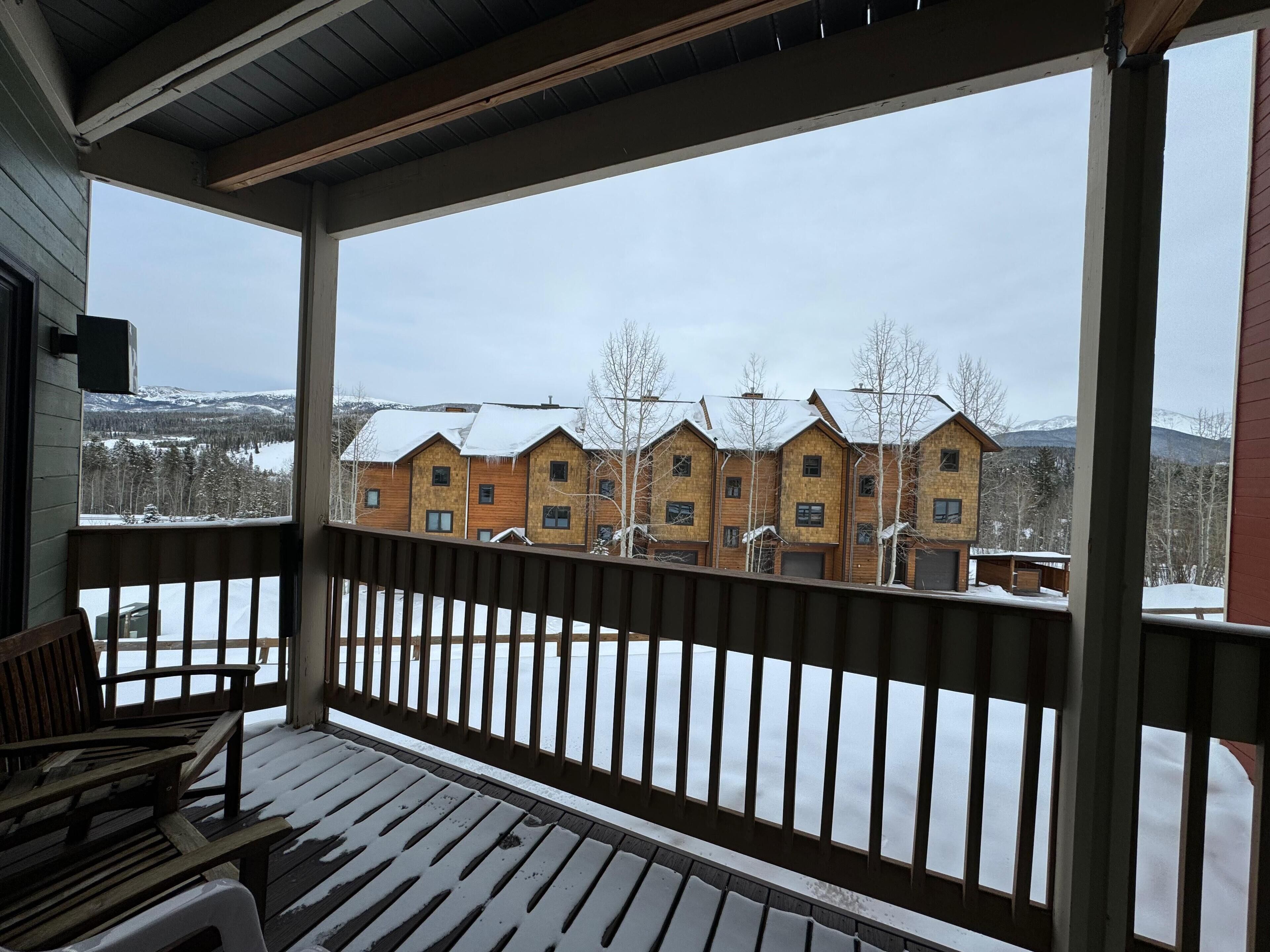 A wooden deck with a railing, a bench, and a view of a row of wooden houses with snow on the ground.