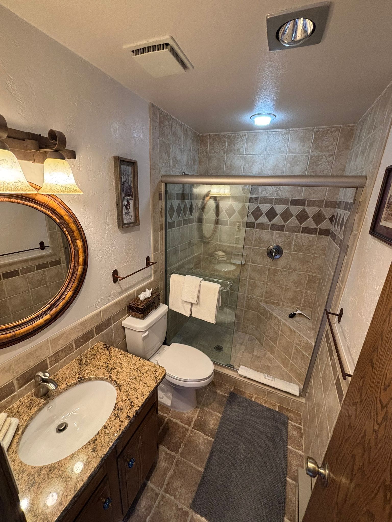 Een badkamer met een wastafel op een granieten blad, een toilet, een douche met glazen wanden en een spiegel met houten lijst.
