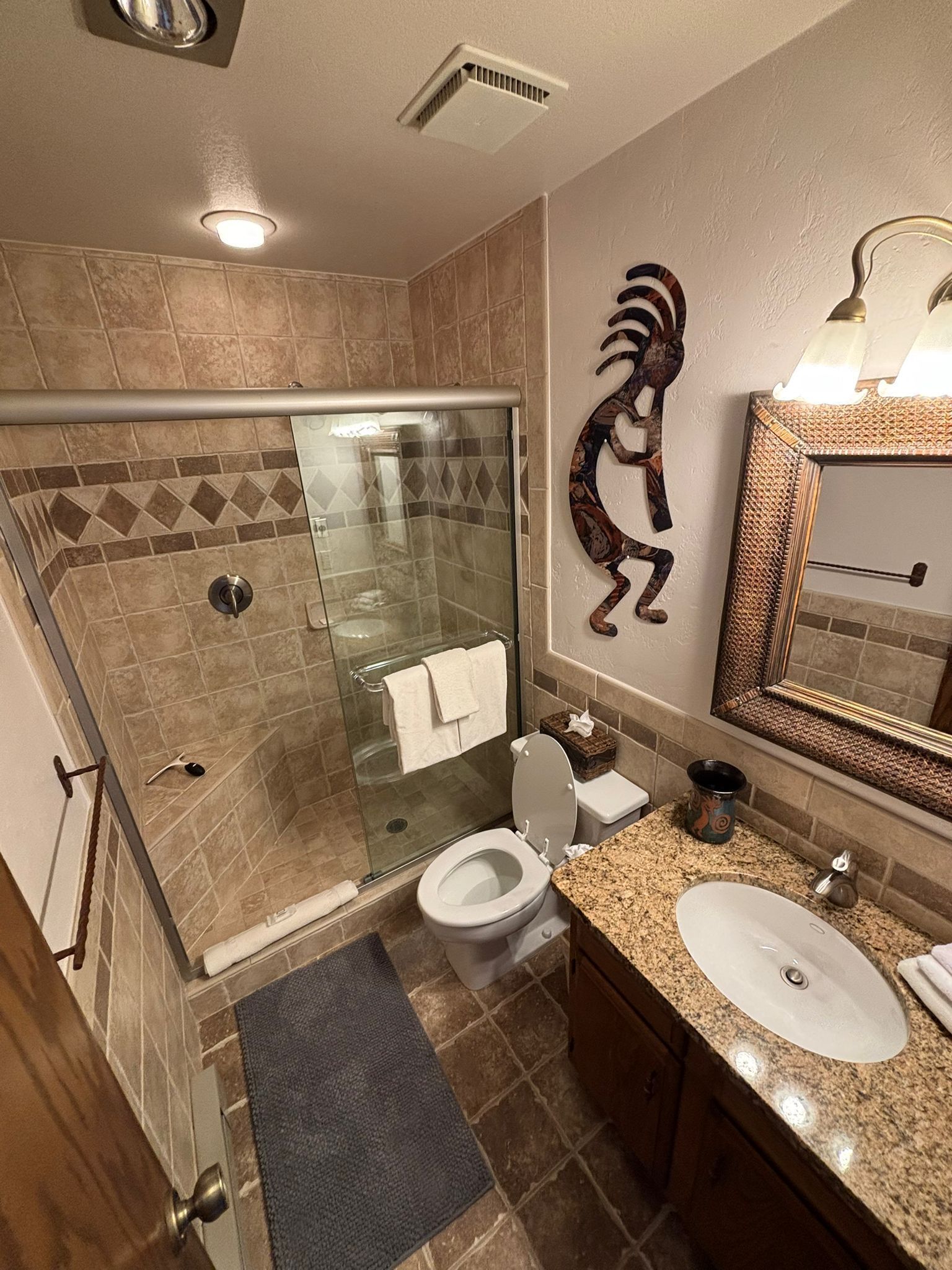 Een moderne badkamer met een glazen douchecabine, toilet, wastafel en spiegel.