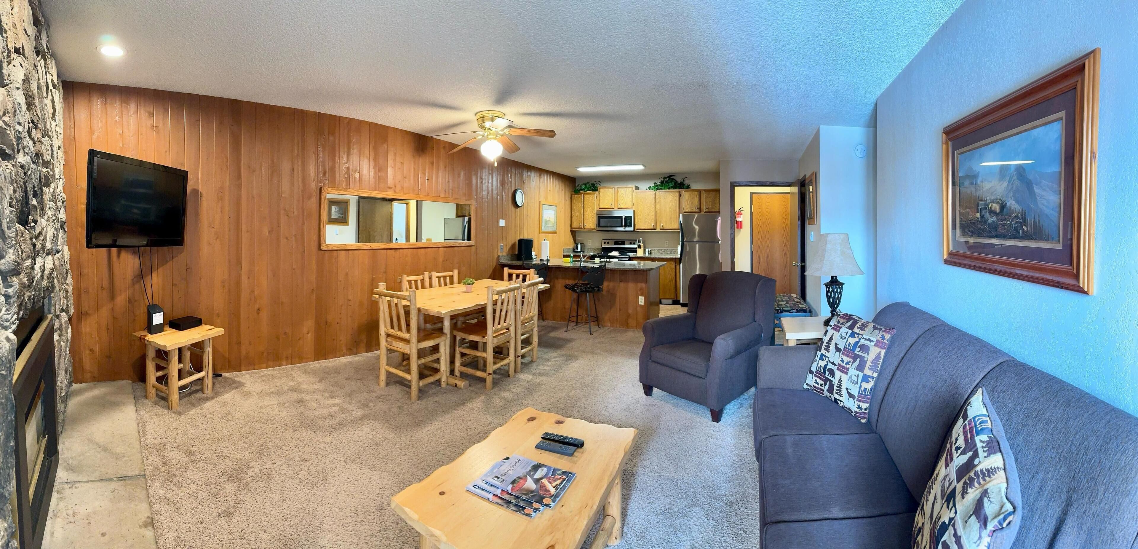 A living room with a wooden dining table, a gray sofa, and a ceiling fan.