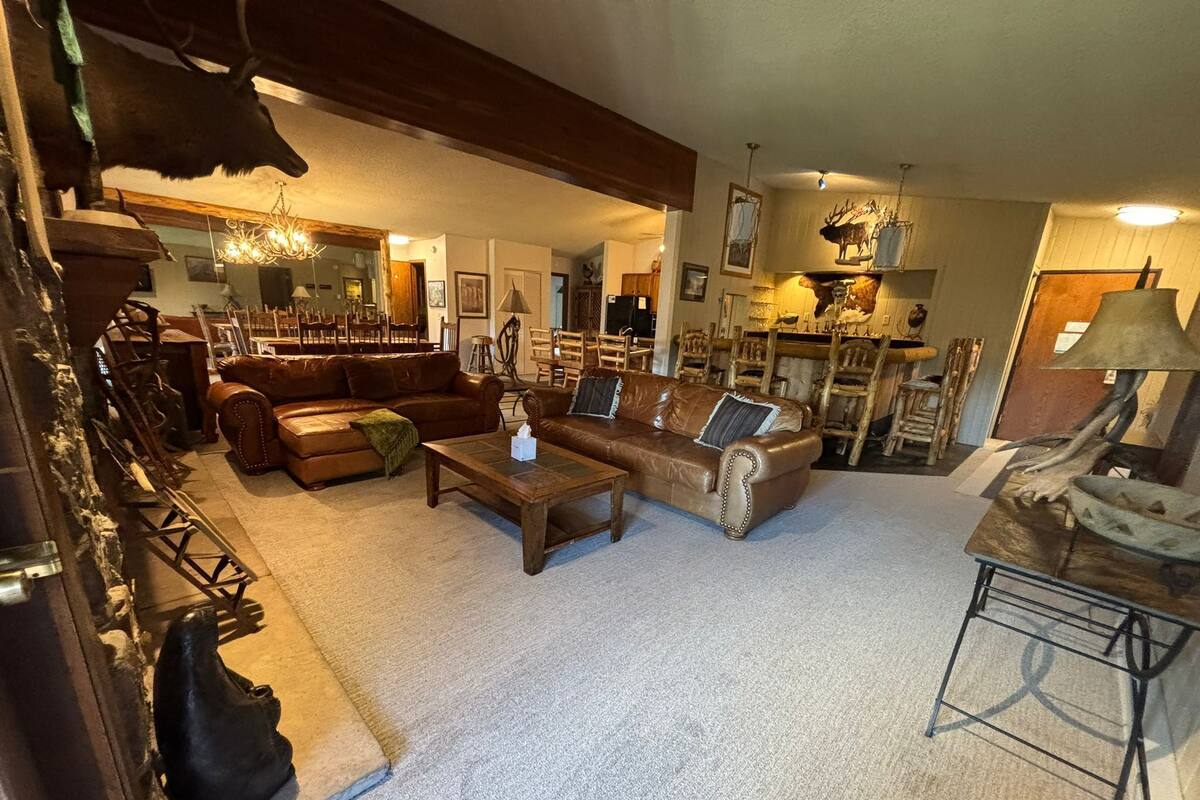 A spacious living room with a large brown leather sofa, a wooden coffee table, and a chandelier.