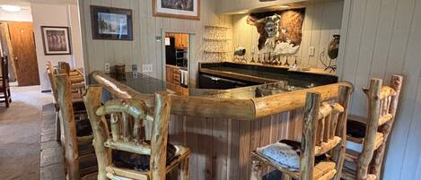 A rustic kitchen with a central island, wooden chairs, and a hanging light fixture.