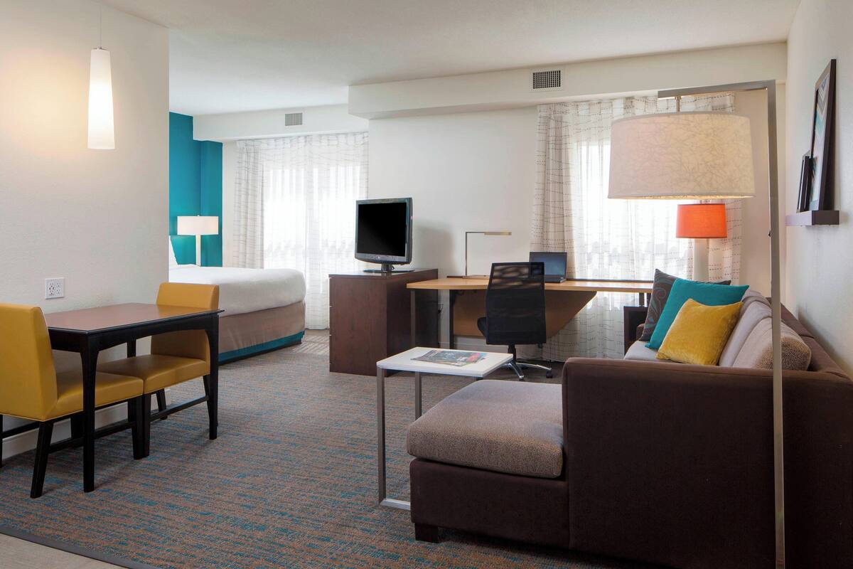 A hotel room with a bed, a desk, a computer, a chair, and a sofa.