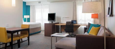 A hotel room with a bed, a desk, a computer, a chair, and a sofa.