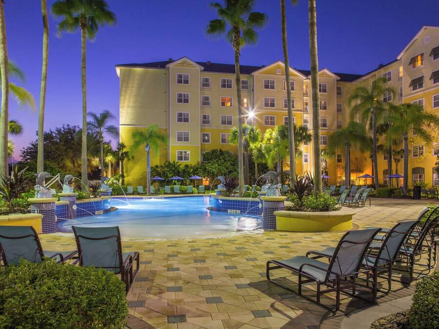 A hotel with a swimming pool, palm trees, and lounge chairs.