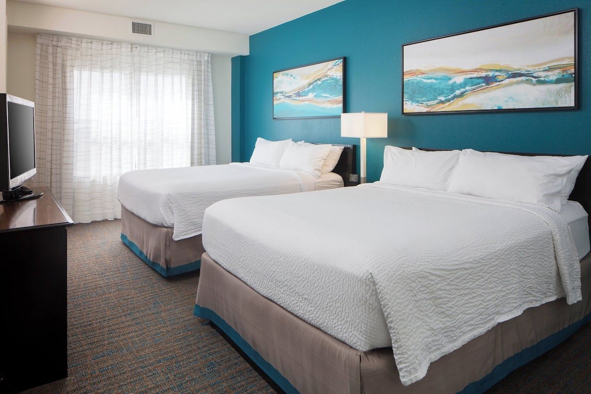 A hotel room with two beds, a television, and artwork on the walls.