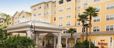 A multi-story hotel with a yellow facade, a covered entrance area, and palm trees.