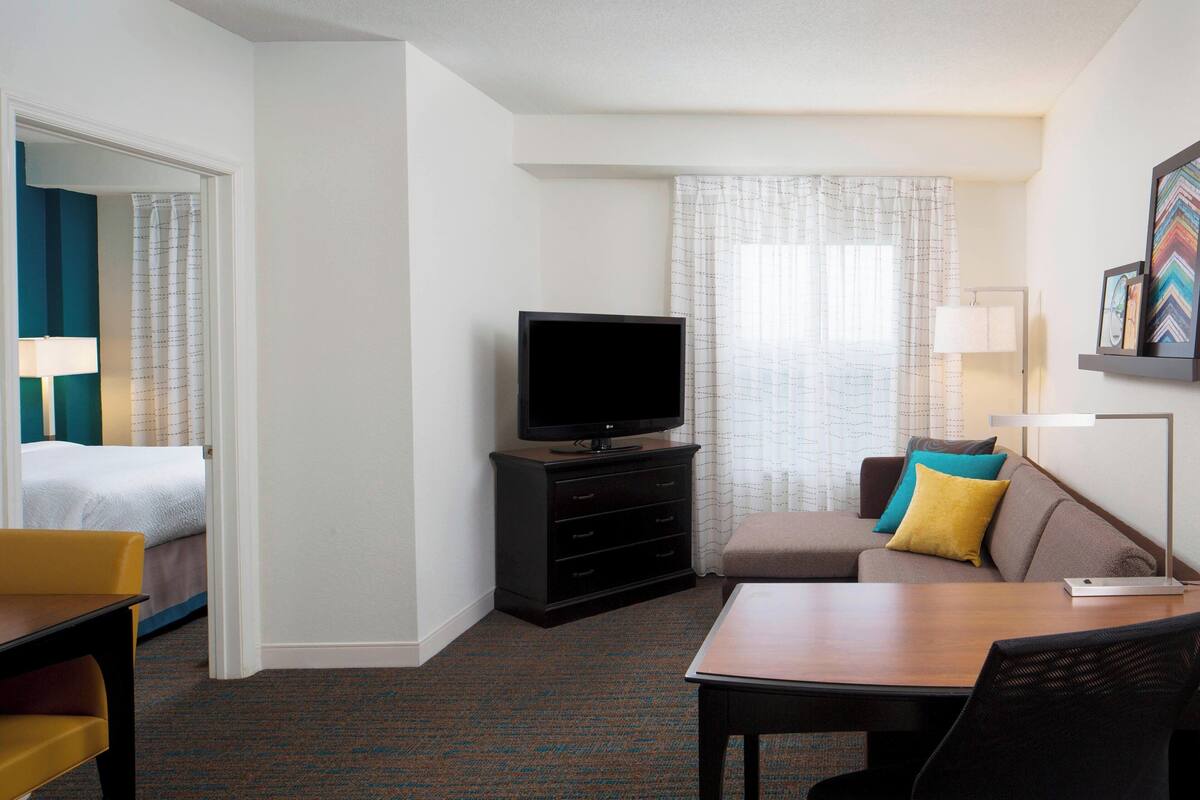 A hotel room with a bed, a TV on a dresser, a sofa, a table, and a lamp.