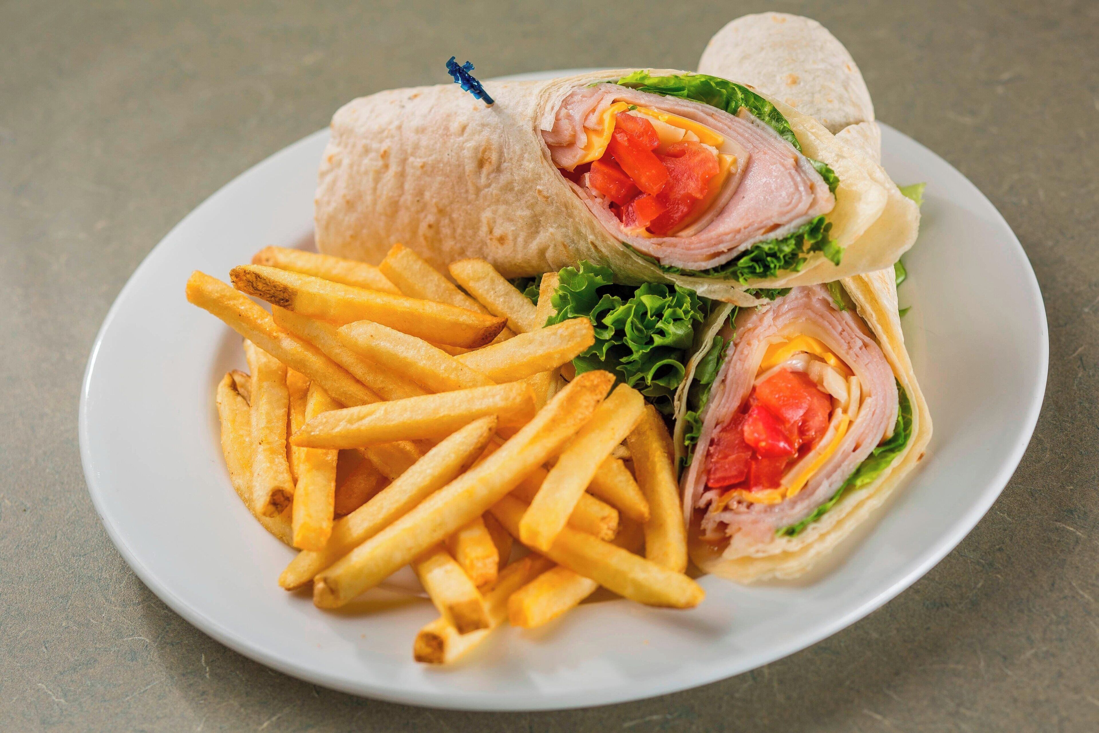 Un piatto con un panino tagliato a metà, patatine fritte e un wrap di tortilla.