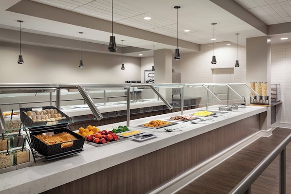 A buffet area with various food options, a glass railing, and hanging pendant lights.