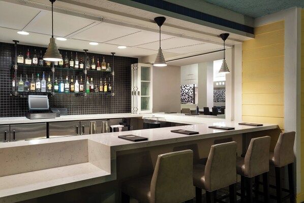 A bar area with a long counter, multiple bar stools, and a variety of liquor bottles on shelves. - Residence Inn by Marriott Orlando at SeaWorld (Orlando)