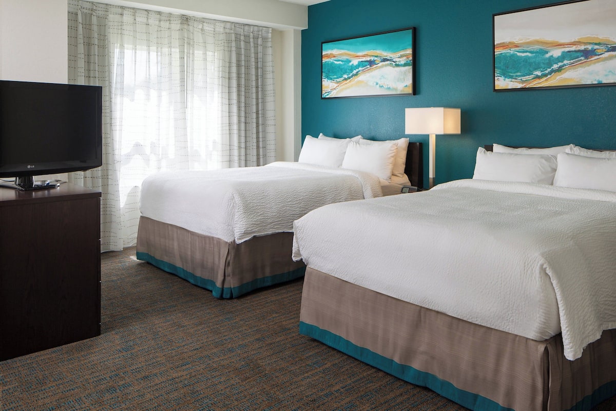 A hotel room with two beds, a TV, and artwork on the walls.