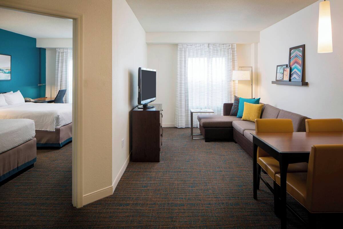 A hotel room with a bed, a sofa, a small table, a TV, and a desk.