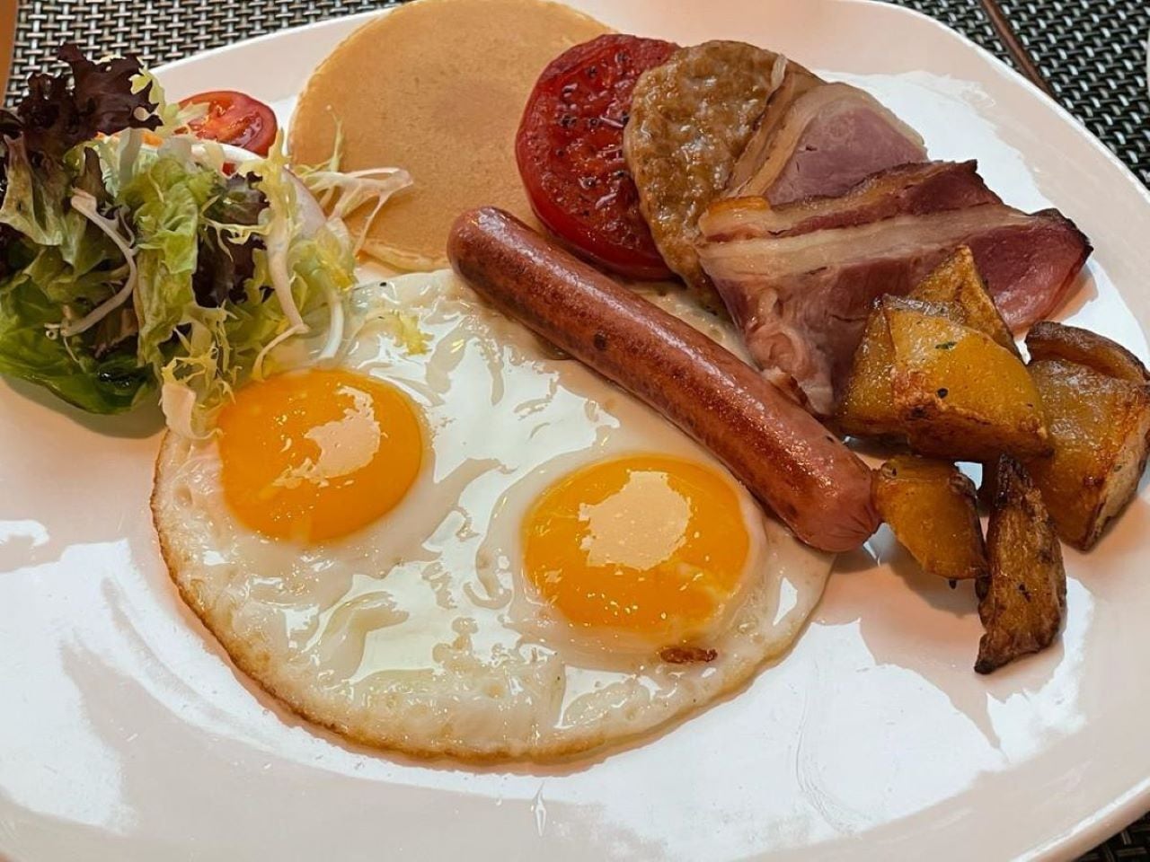 Une assiette composée d’œufs, de bacon, de saucisses, de pommes de terre et d’une salade en accompagnement.