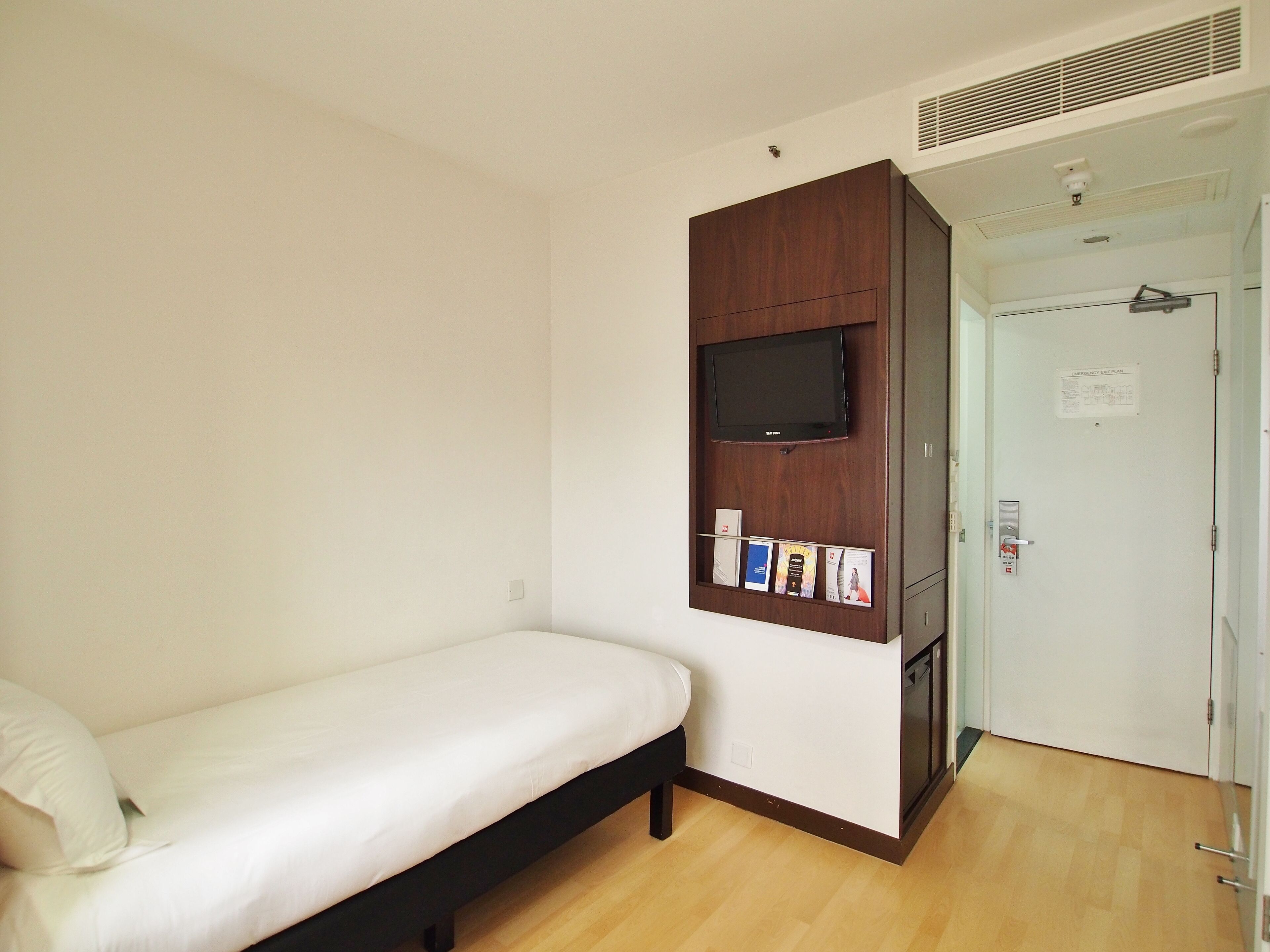 A bedroom with a bed, a mounted TV, and a door with an emergency exit plan.