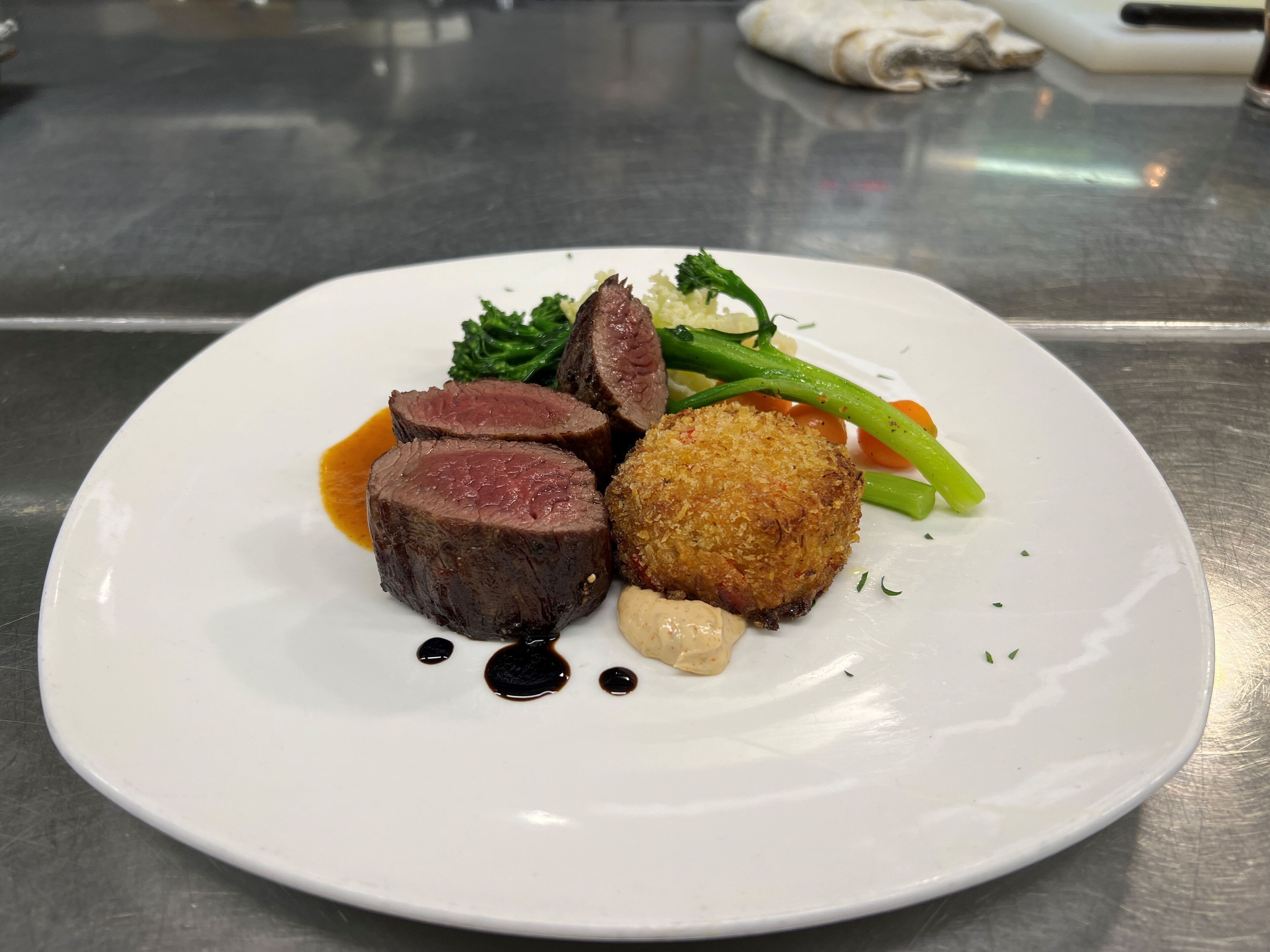 A plate of food with sliced meat, a breaded item, and vegetables.