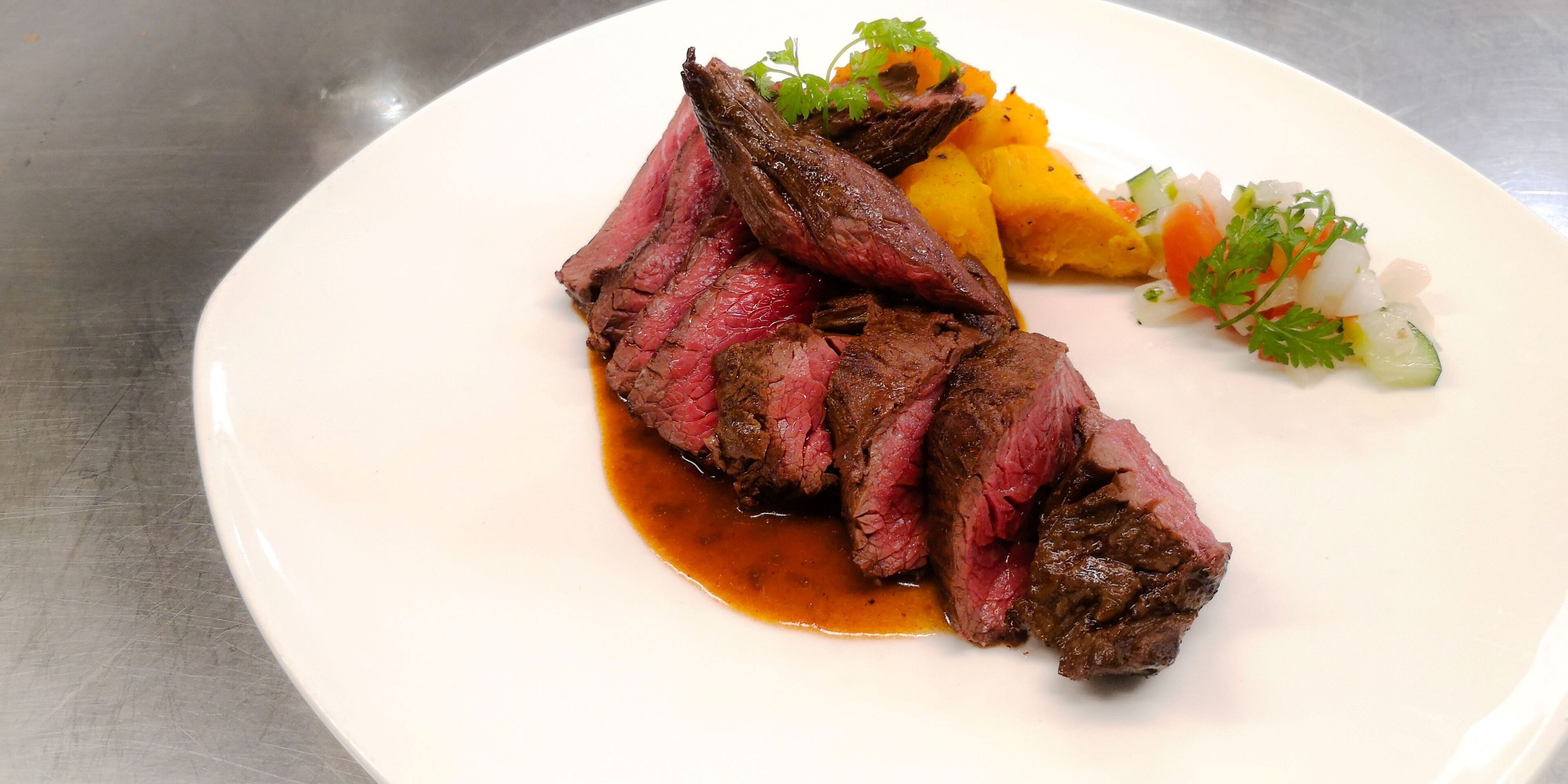 A plate with sliced steak, a side of roasted vegetables, and a small salad.