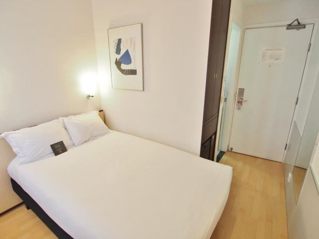A hotel room with a large bed, a wall-mounted light, and a door with a sign.