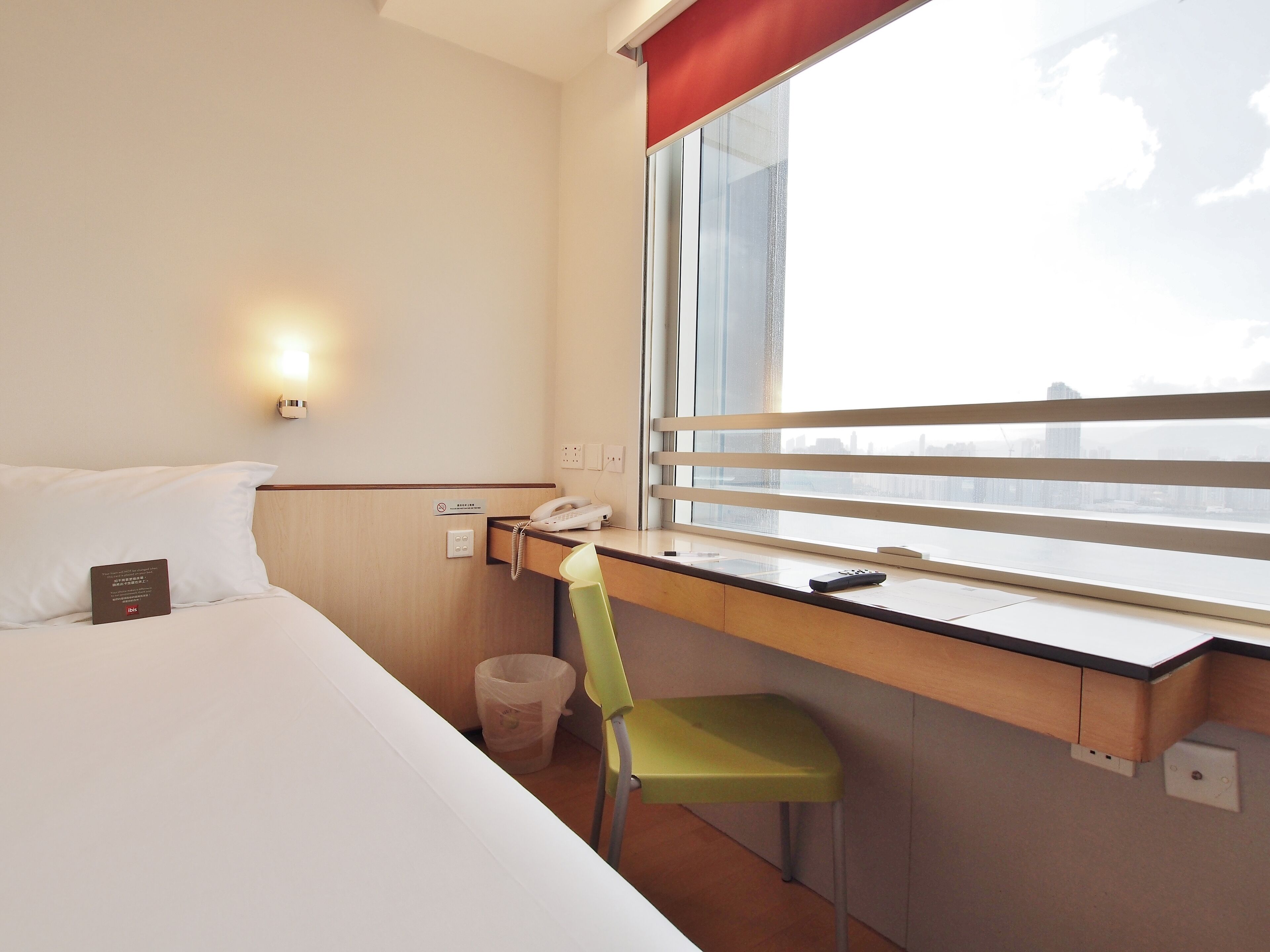 A hotel room with a bed, a desk with a telephone, a chair, and a window with a view of the city skyline.