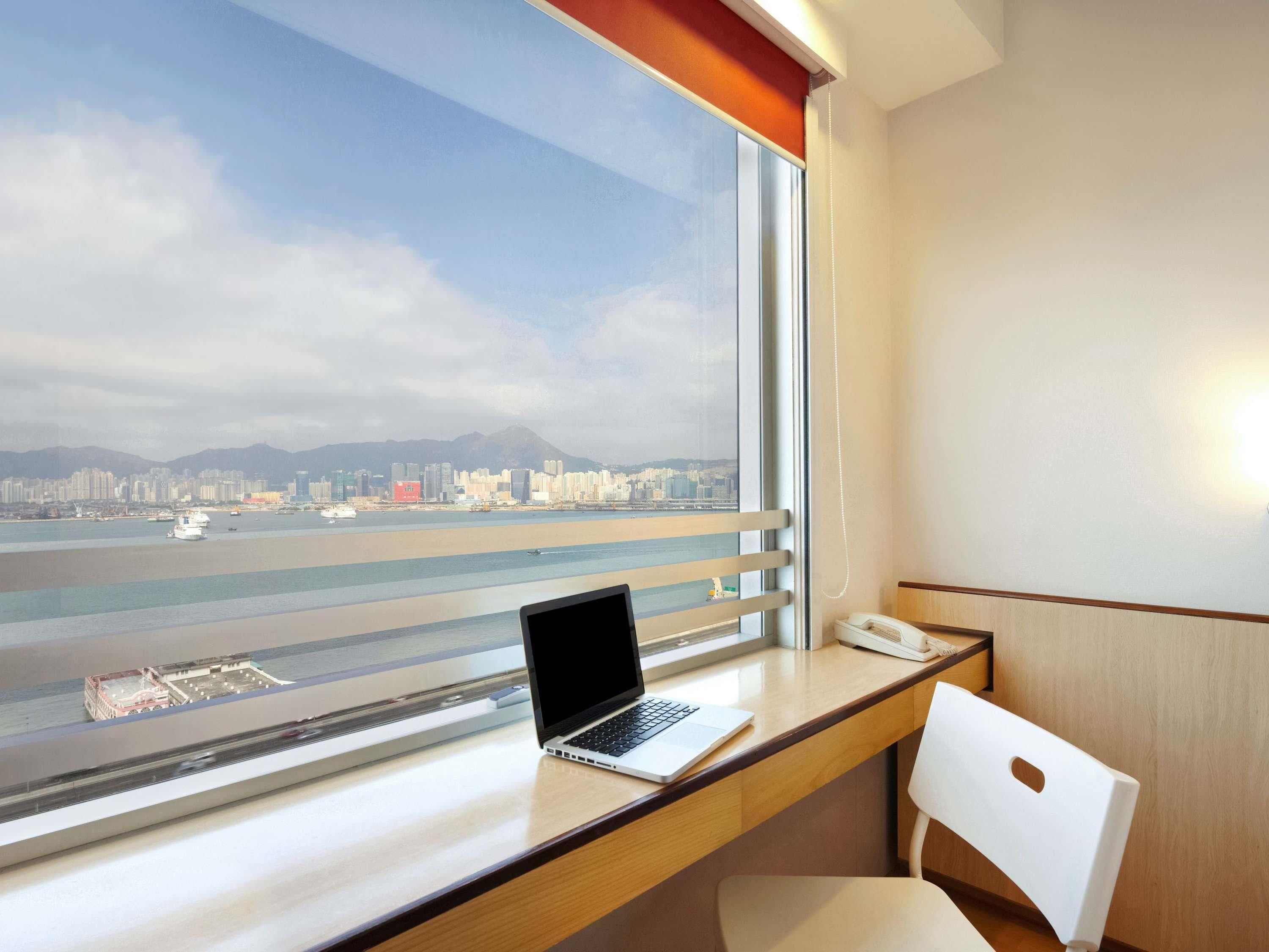 Une chambre d’hôtel équipée d’un bureau, d’un ordinateur portable, d’une chaise et offrant une vue sur le paysage urbain et l’eau.