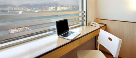 Habitación de hotel con escritorio, computadora portátil, silla y vista a la ciudad y al agua.
