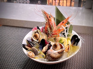 Una bandeja de mariscos con diversos crustáceos y un camarón decorativo sobre una estera trenzada.