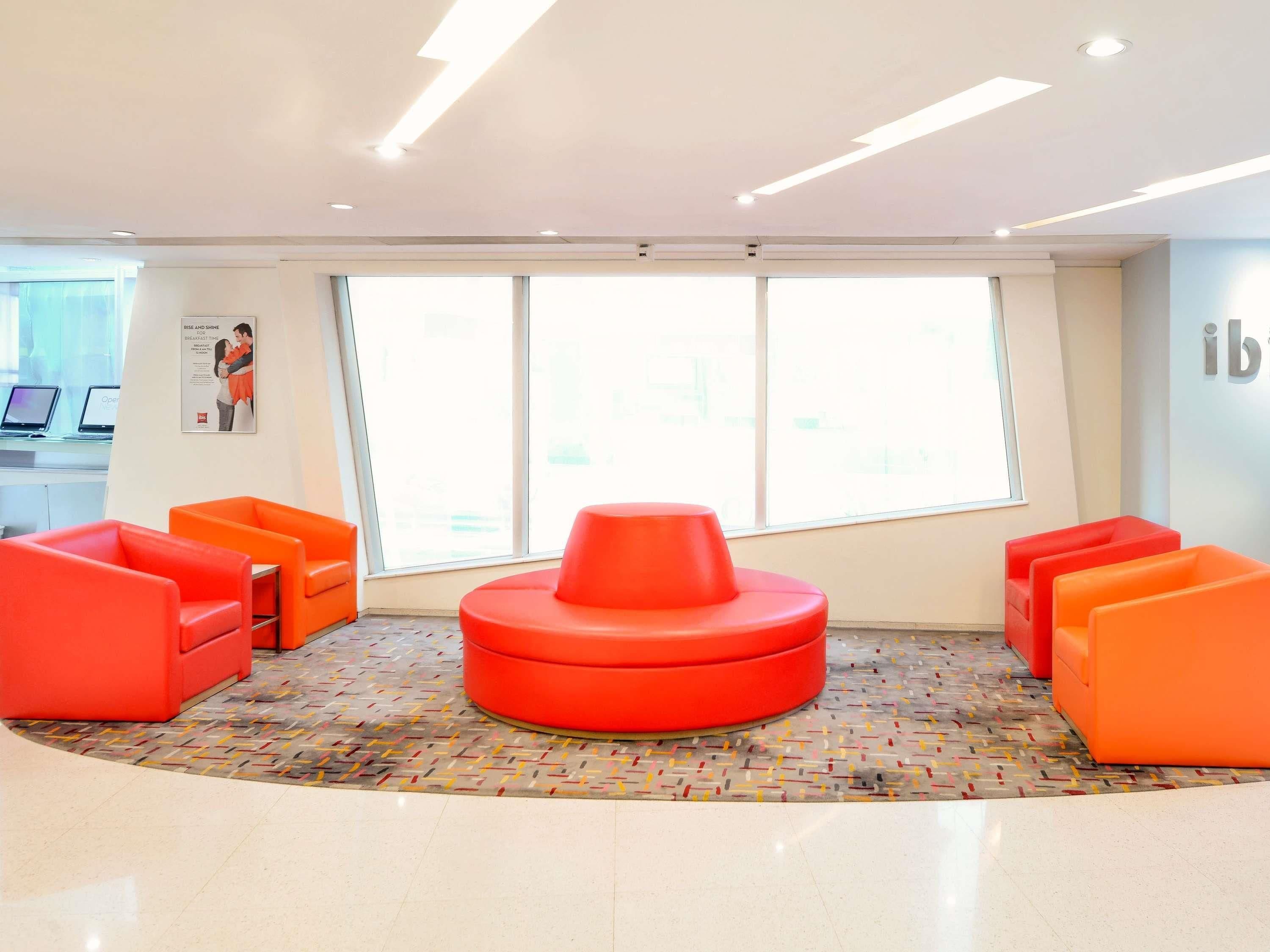 Zona de espera moderna con asientos color naranja brillante, ventanas amplias y un letrero visible que dice 'ib'.