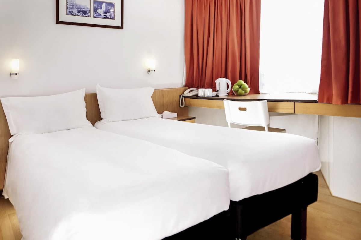 A hotel room with two beds, a desk, a chair, a telephone, and a framed picture on the wall.