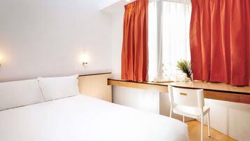 A hotel room with a large bed, a desk, and a window with curtains.