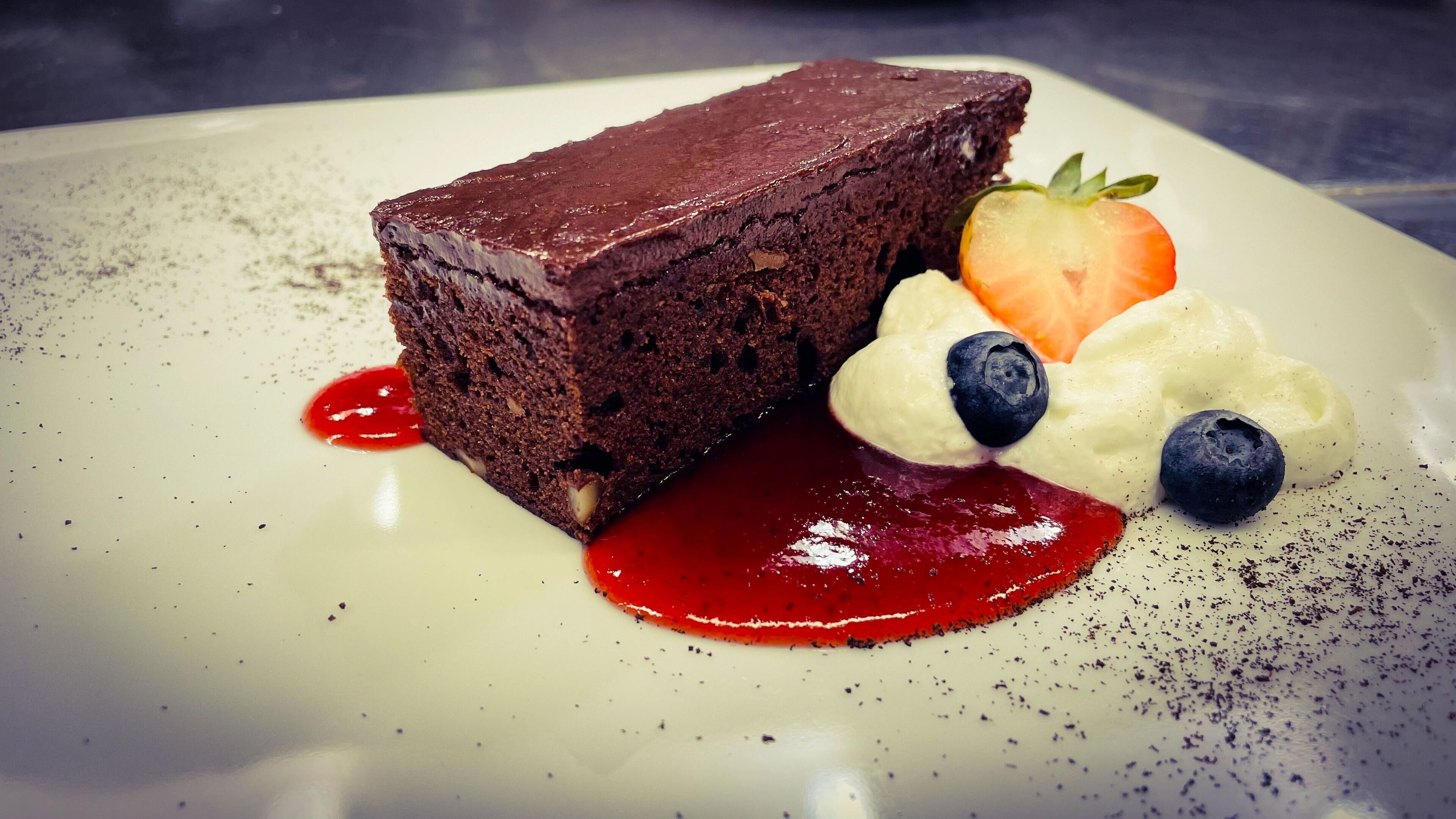 En efterrätt bestående av chokladkaka, jordgubbar, blåbär och vispad grädde, serverad på en tallrik.