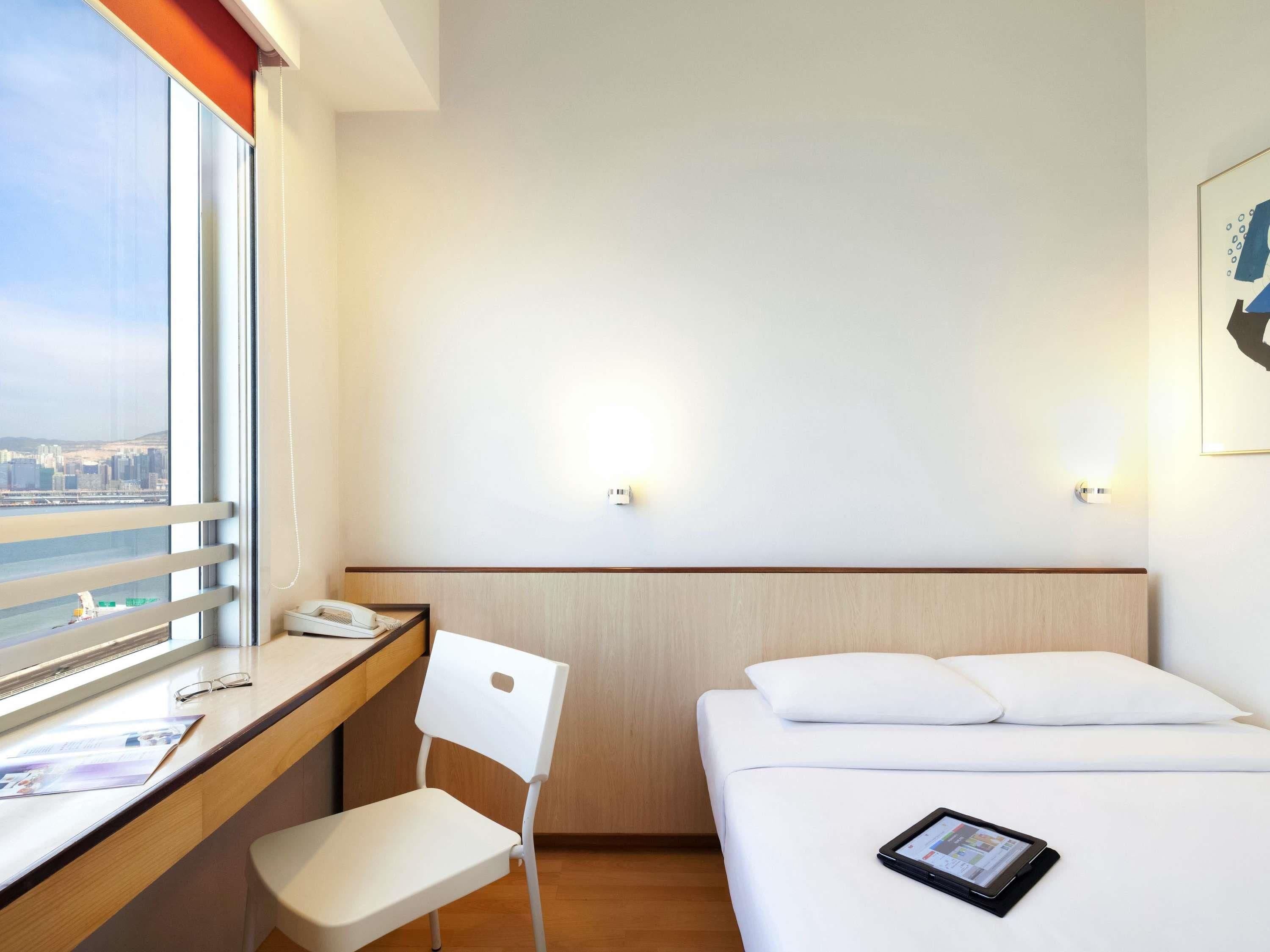 Hotelkamer met een bed, een bureau met stoel, een telefoon en een tablet op het bed.