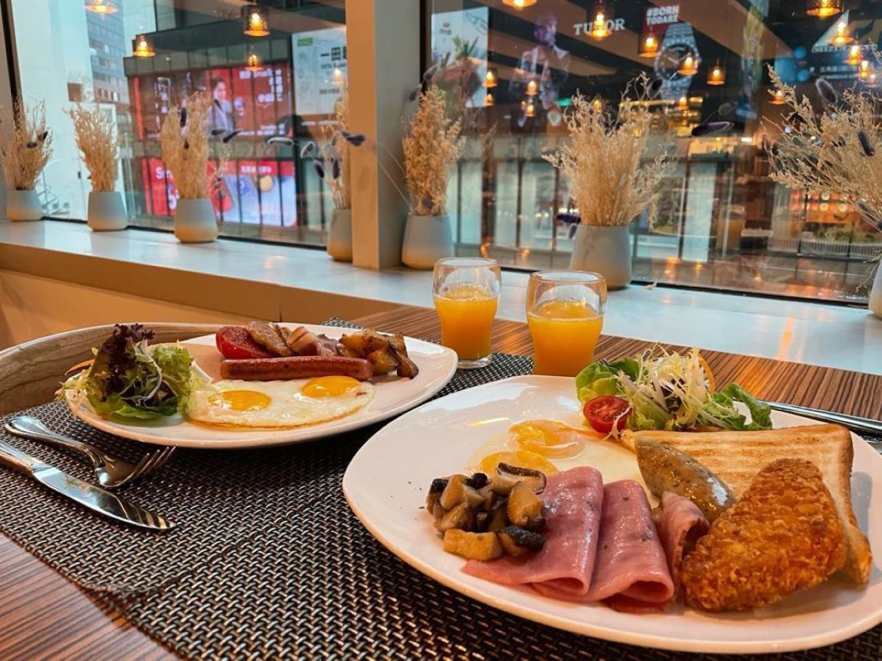 A breakfast setting with plates of eggs, bacon, mushrooms, ham, and toast, along with a side salad and orange juice.