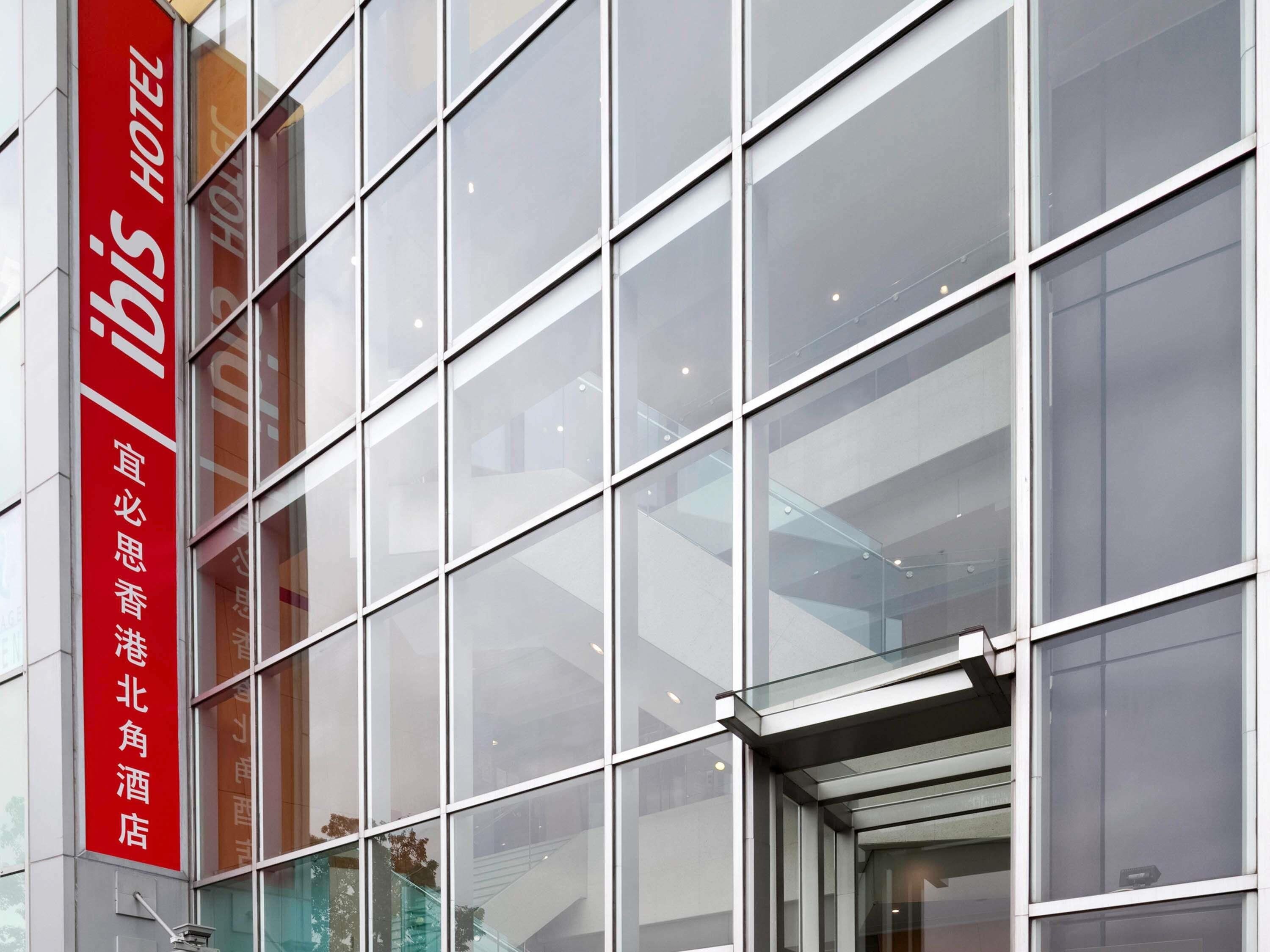 A modern building facade with large glass windows and a prominent red vertical sign with white text.