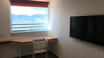 A room with a desk, a chair, a TV, and a window with a view of a cityscape.