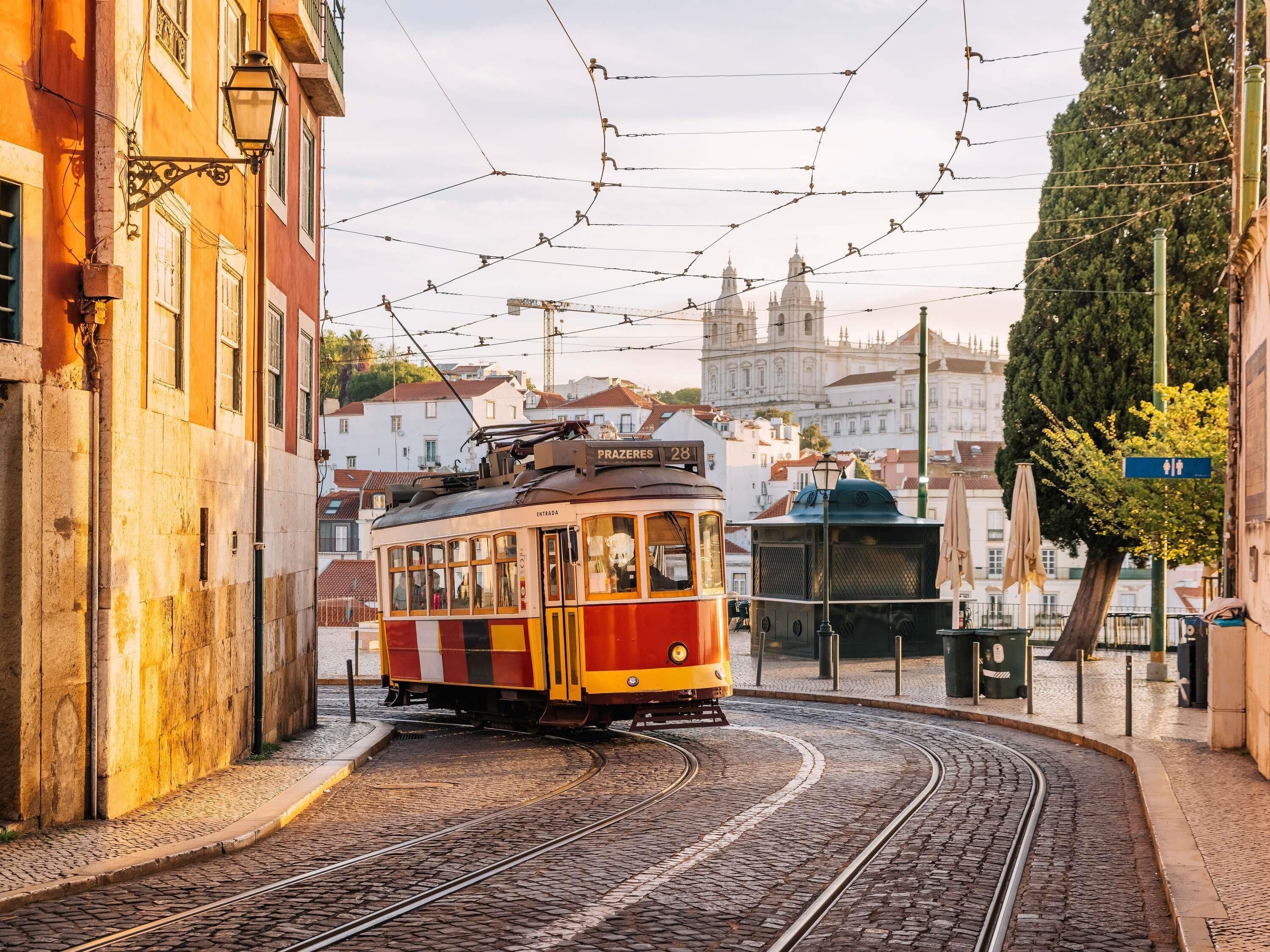 Eine Straßenbahn auf einer Kurve in einer Stadt mit Gebäuden und einer großen Kirche im Hintergrund.