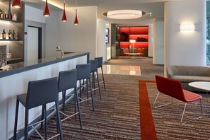 Un moderno vestíbulo de hotel con área de bar, asientos y una pared de acento roja.