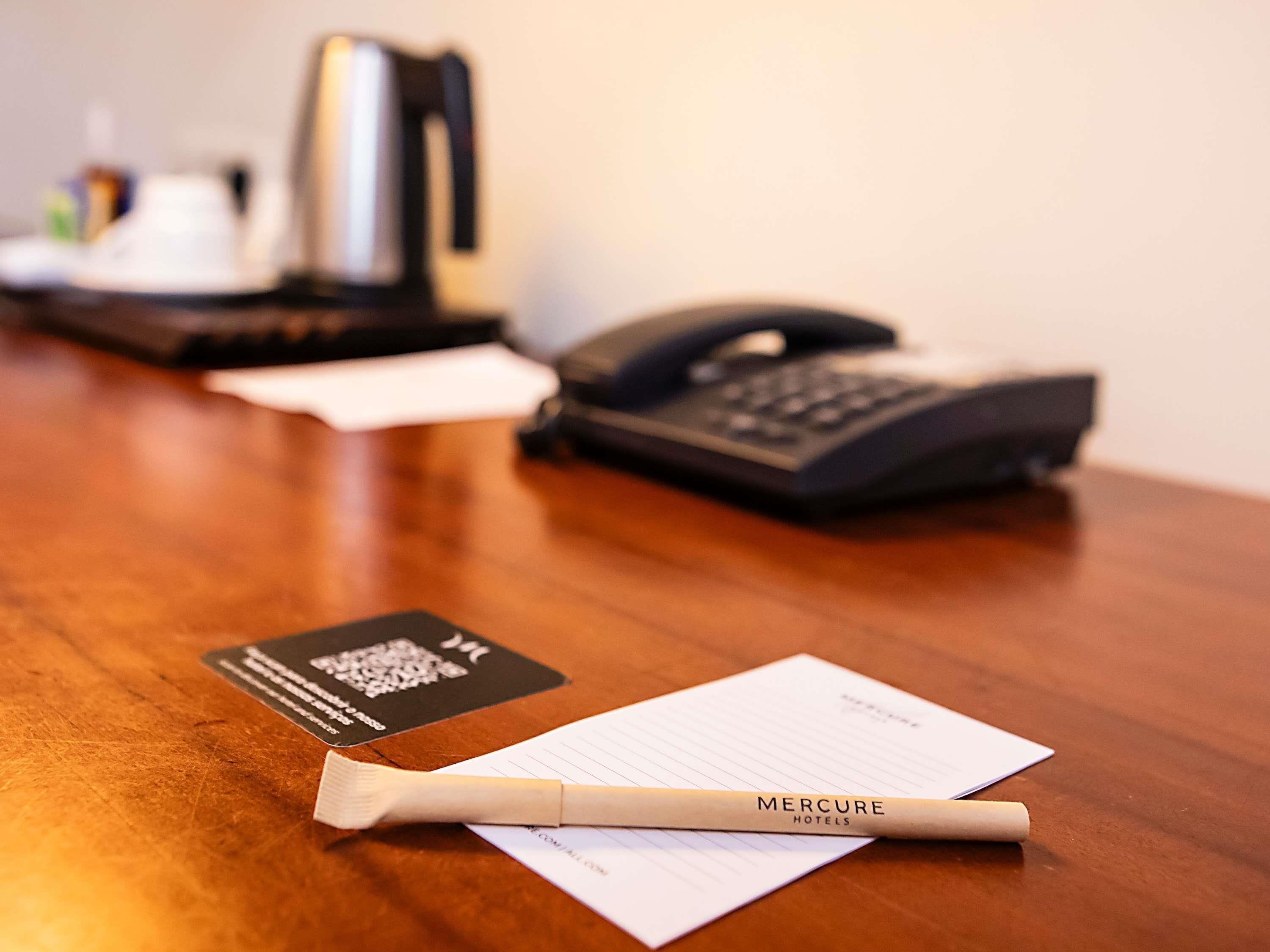 Uma mesa de madeira com uma caneta, um cartão de visita e um bloco de notas.