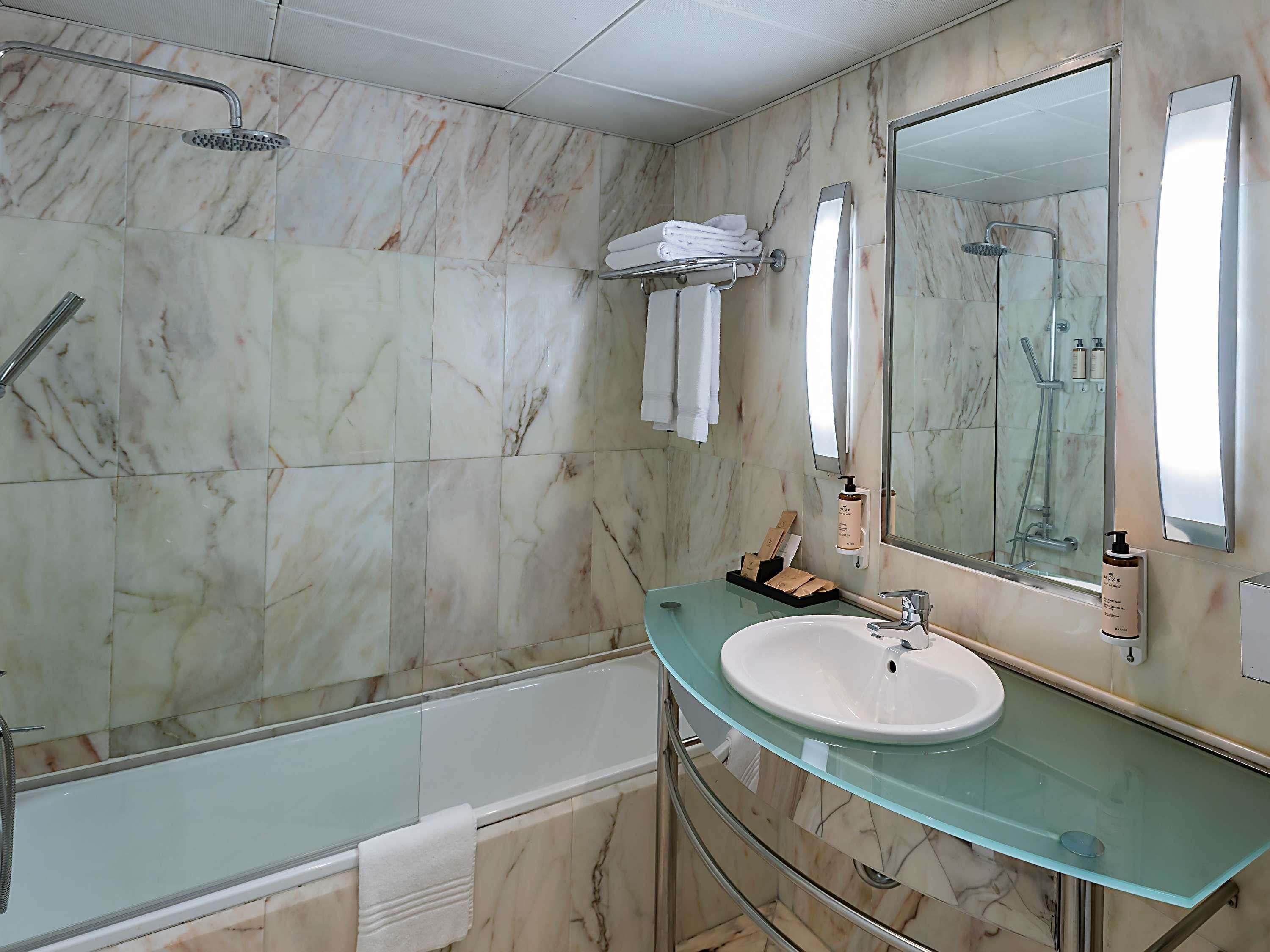 A bathroom with a glass sink, a bathtub, and a shower area.