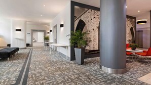 A modern hotel lobby with a patterned carpet, seating areas, and a brick wall accent. - Mercure Lisboa Hotel (Lisbon)